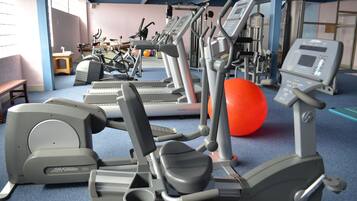 Un gimnasio con diversas máquinas de ejercicio, incluyendo cintas de correr y elípticas, y una pelota de ejercicios roja.