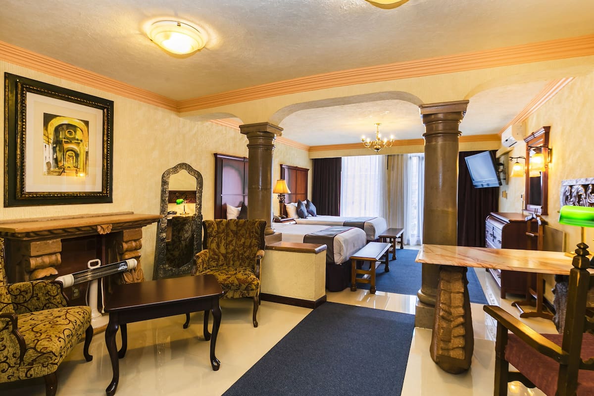 A hotel room with a large bed, two bedside tables, a desk, a chair, a mirror, and a fireplace.