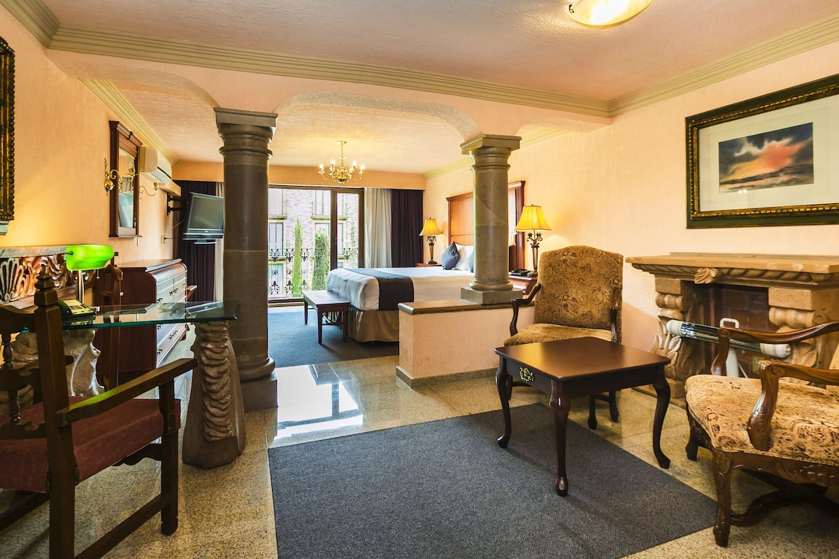 A hotel room with a bed, a desk, a chair, a fireplace, and a view of the outdoors.