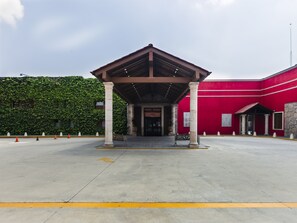 A building with a red facade, a covered entrance, and a paved area with yellow lines.