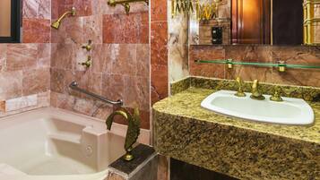 Une salle de bain avec un mur recouvert de carreaux de marbre, une baignoire, un lavabo sur un plan de travail en granit et des accessoires dorés.