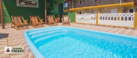 Una piscina con cuatro sillas de madera para tomar el sol.
