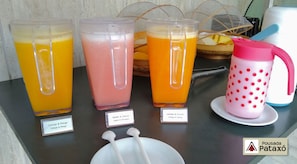 A selection of fruit juices in dispensers with labels indicating flavors like orange & mango, guava & pineapple, and laranja & mamão orange & papaya.