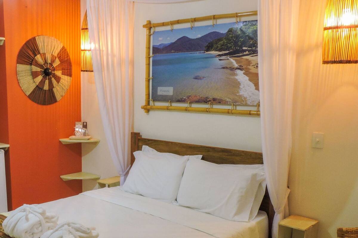 A hotel room with a bed, a wall clock, a small table, and a picture of a beach.