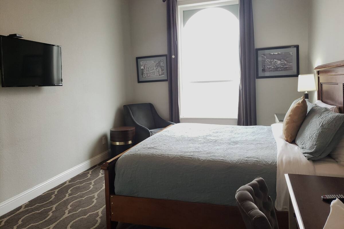 A hotel room with a bed, a chair, a desk, a television, and a window with curtains.