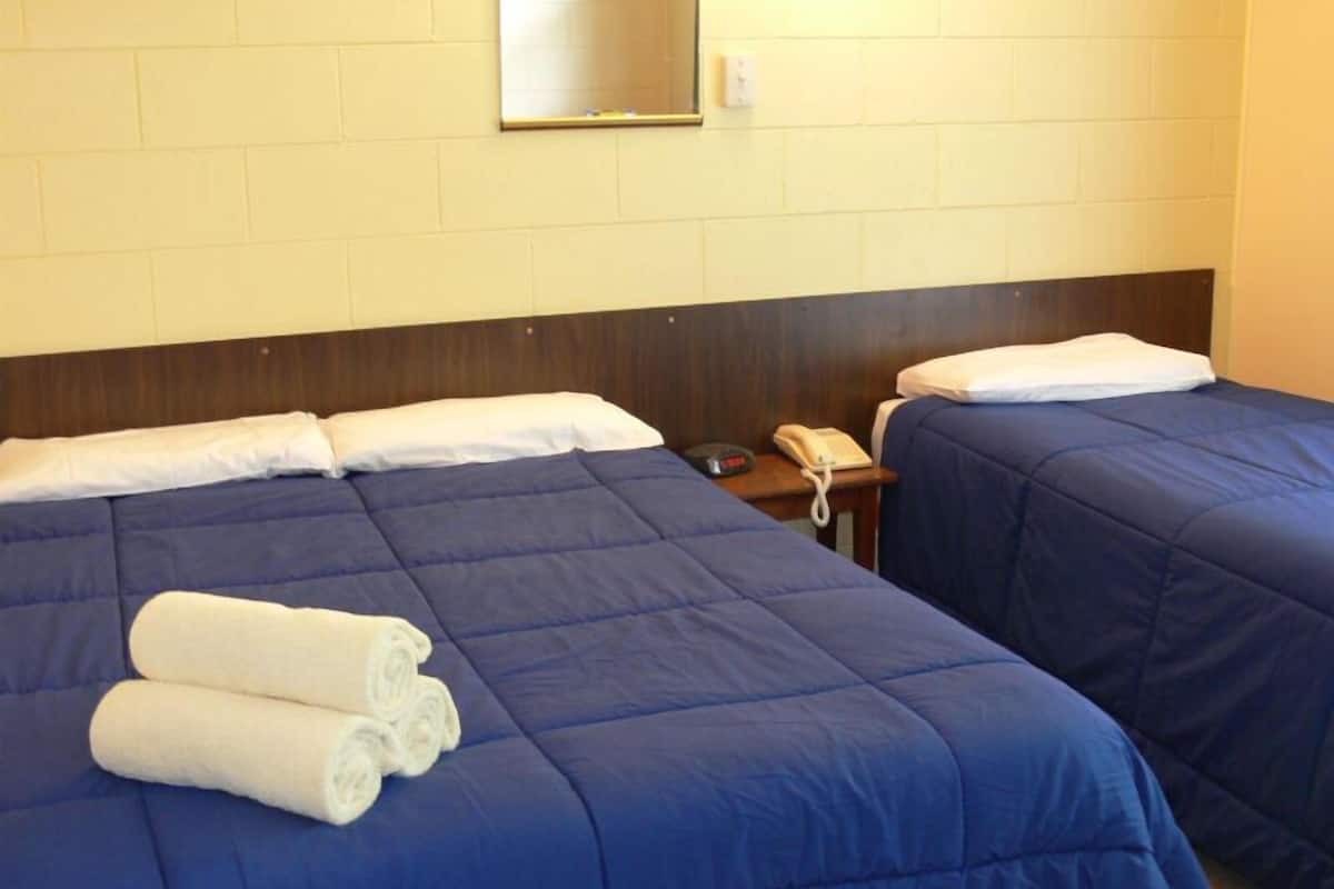 A hotel room with two beds, each with a blue bedspread and white pillows. There is a bedside table with a telephone and a mirror on the wall.