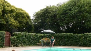 A swimming pool with people in the water and a table with an umbrella in the background. - Glowworm Motel (Hangatiki)
