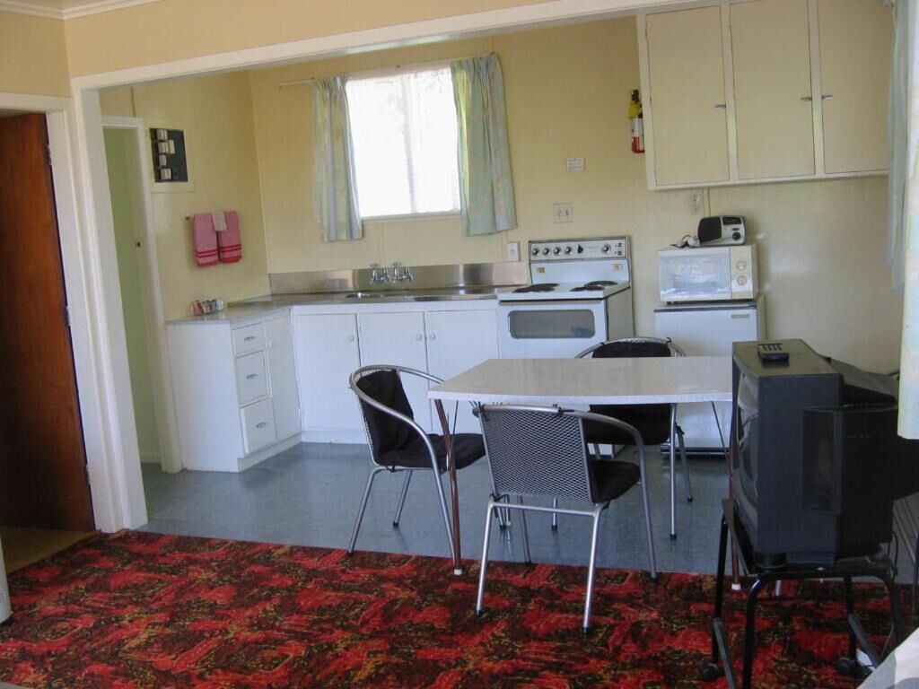 A compact kitchen with white cabinets, a stove, a microwave, and a television on a stand. There are two chairs around a small table.