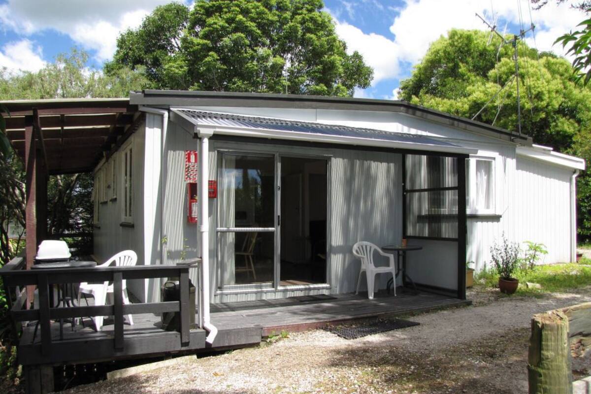 A small, single-story building with a covered porch, a sliding glass door, and a small patio area with a table and chairs.