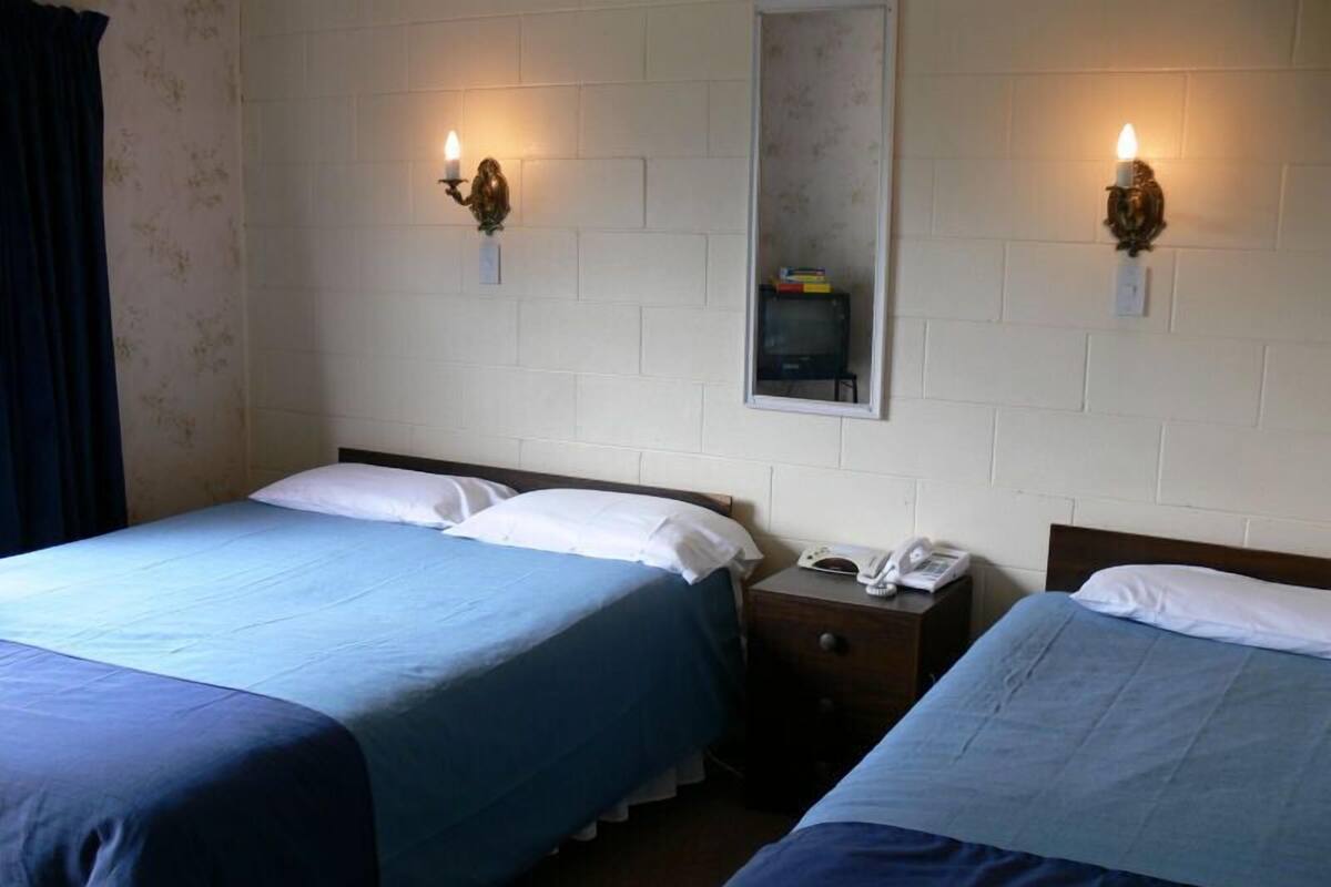 A hotel room with two beds, a bedside table with a phone, and wall-mounted lamps.