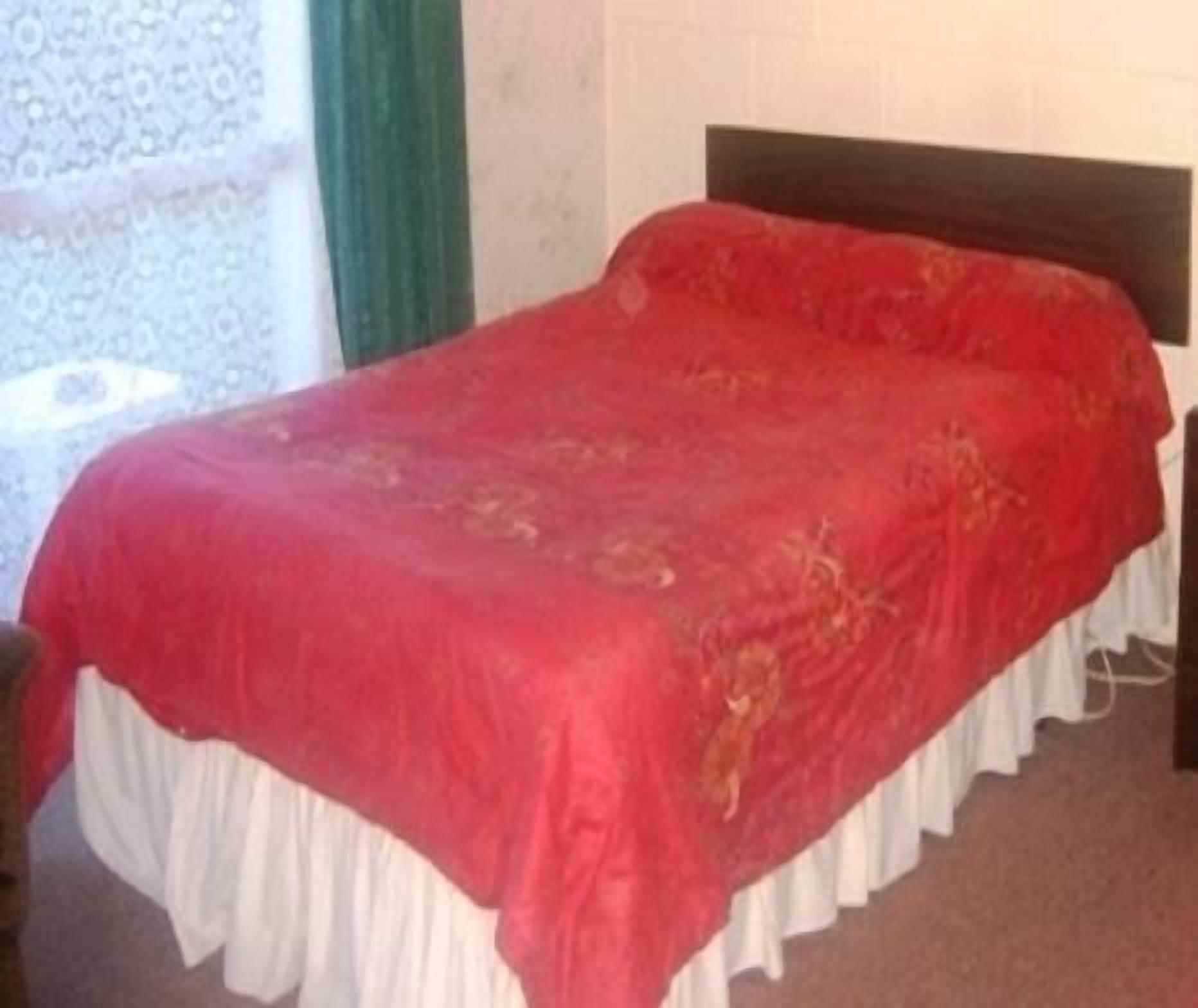 A bed with a red bedspread and white skirted legs.