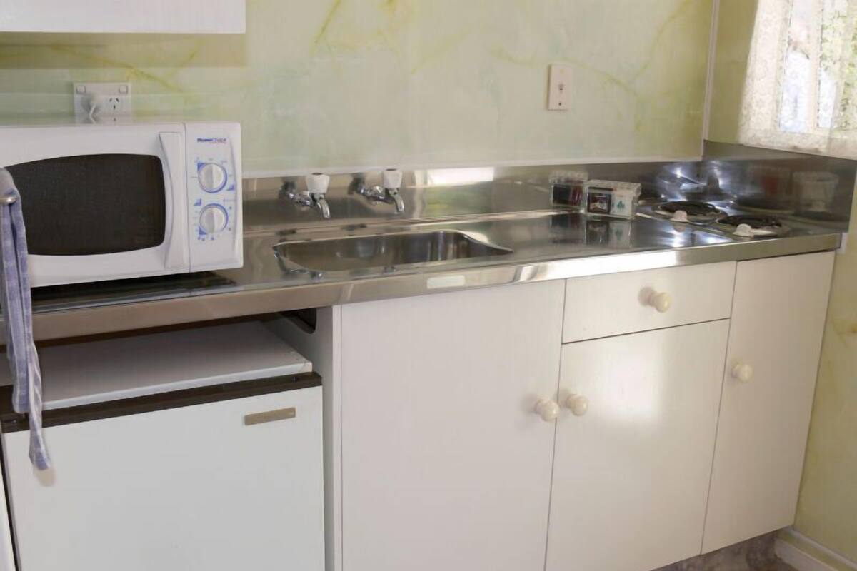 A kitchen with a microwave, stainless steel sink, and white cabinets.