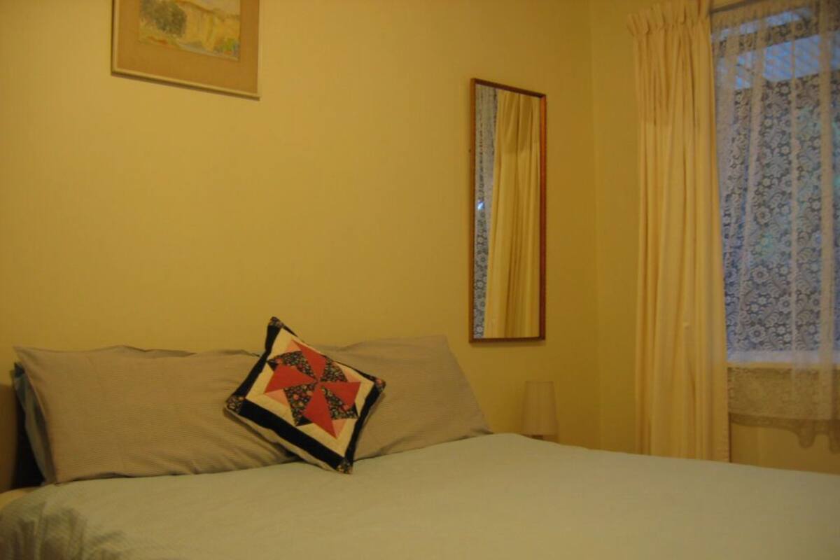 A bed with a quilted pillow, a framed picture on the wall, and a window with curtains.