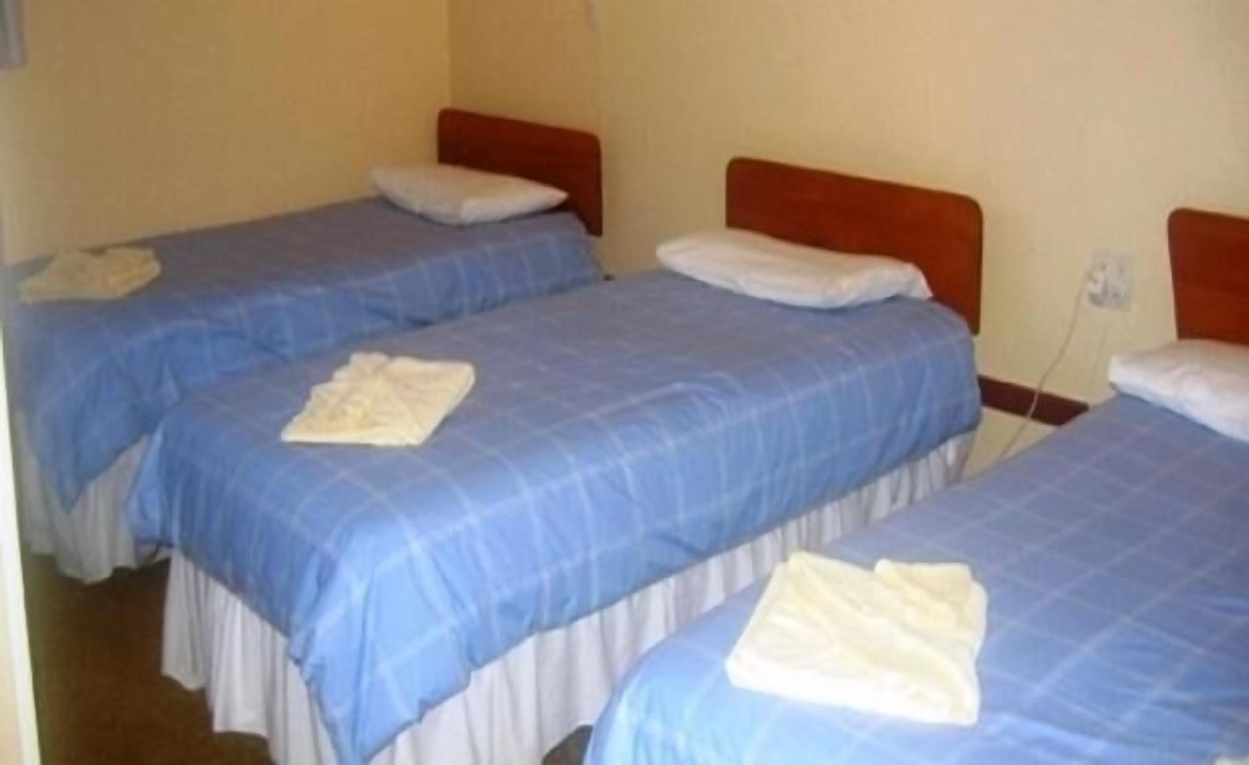 A room with three single beds, each with a blue bedspread and white pillows.