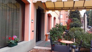 A hotel entrance with a sign reading "HOTEL ALEXA". There are outdoor seating areas with tables and chairs, and a potted plant with flowers on the left. - Hotel Alexander (Fiorano Modenese)