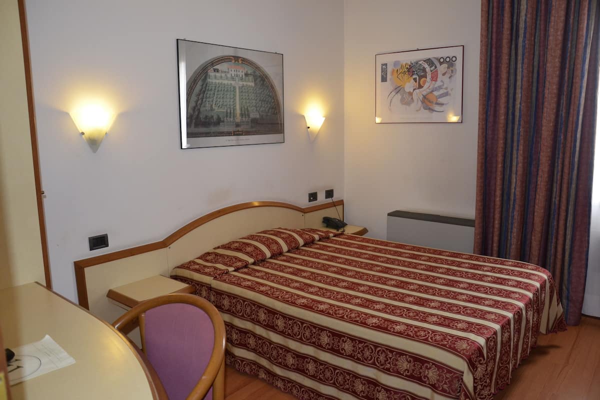 A hotel room with a bed, a desk, a chair, and two wall-mounted light fixtures.