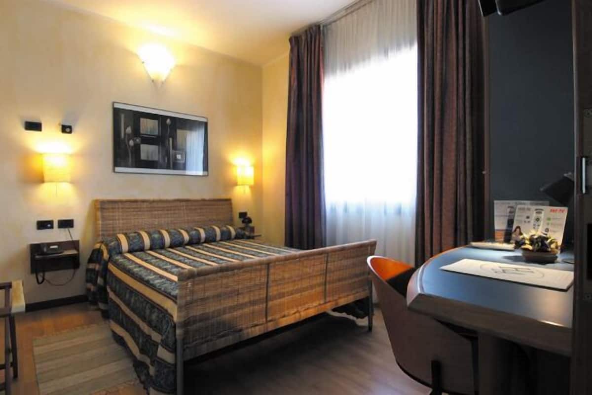 A hotel room with a bed, a desk, and a TV.