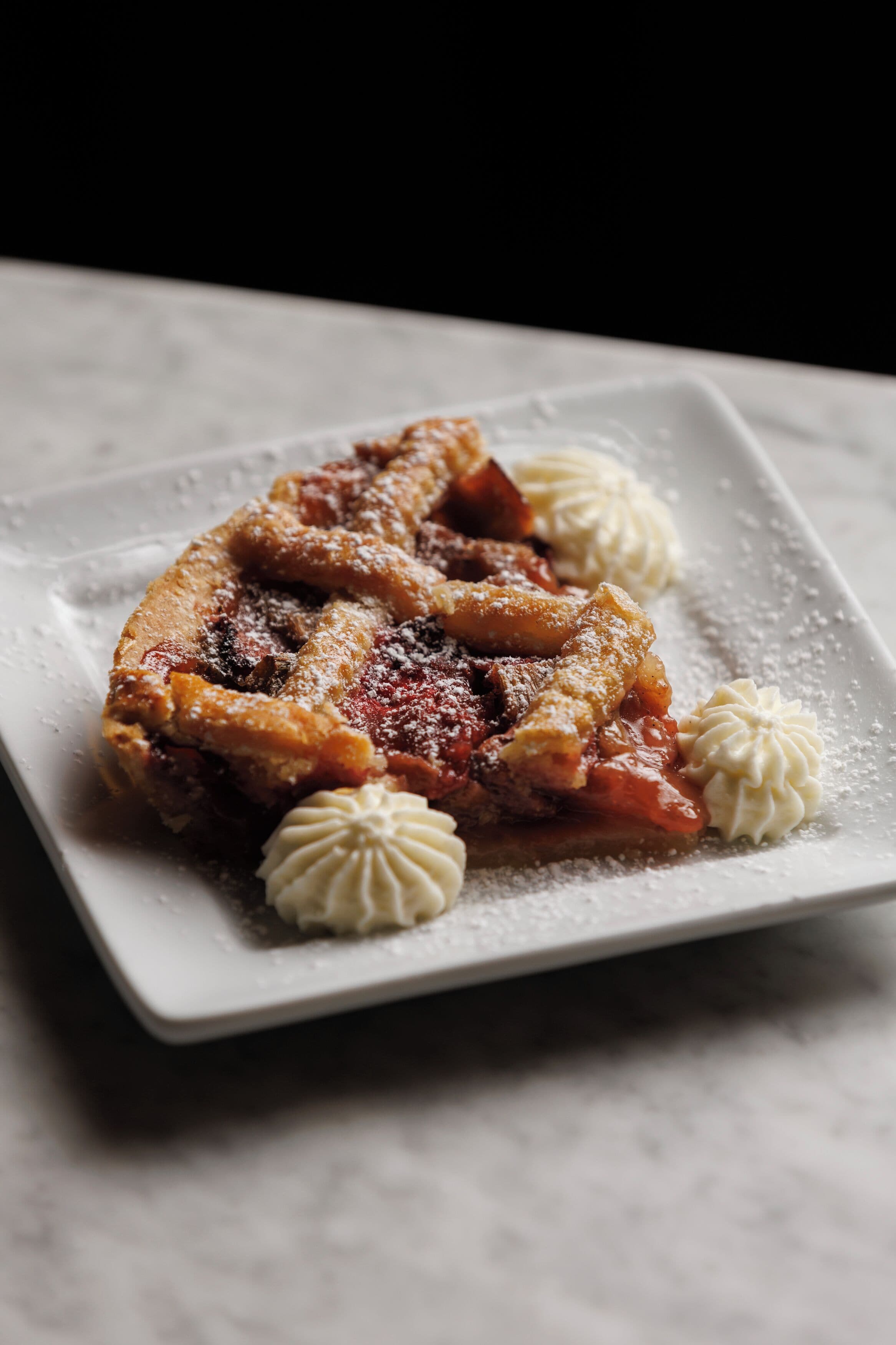 A dessert plate with a pie, whipped cream, and powdered sugar.