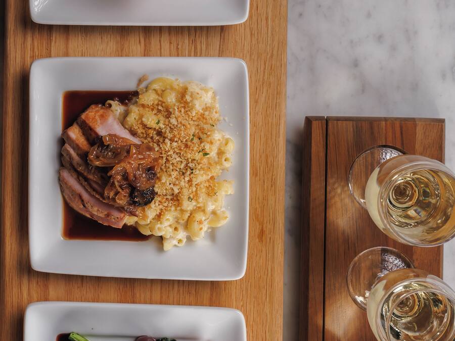 Three plates of food on a wooden table with two glasses of white wine.
