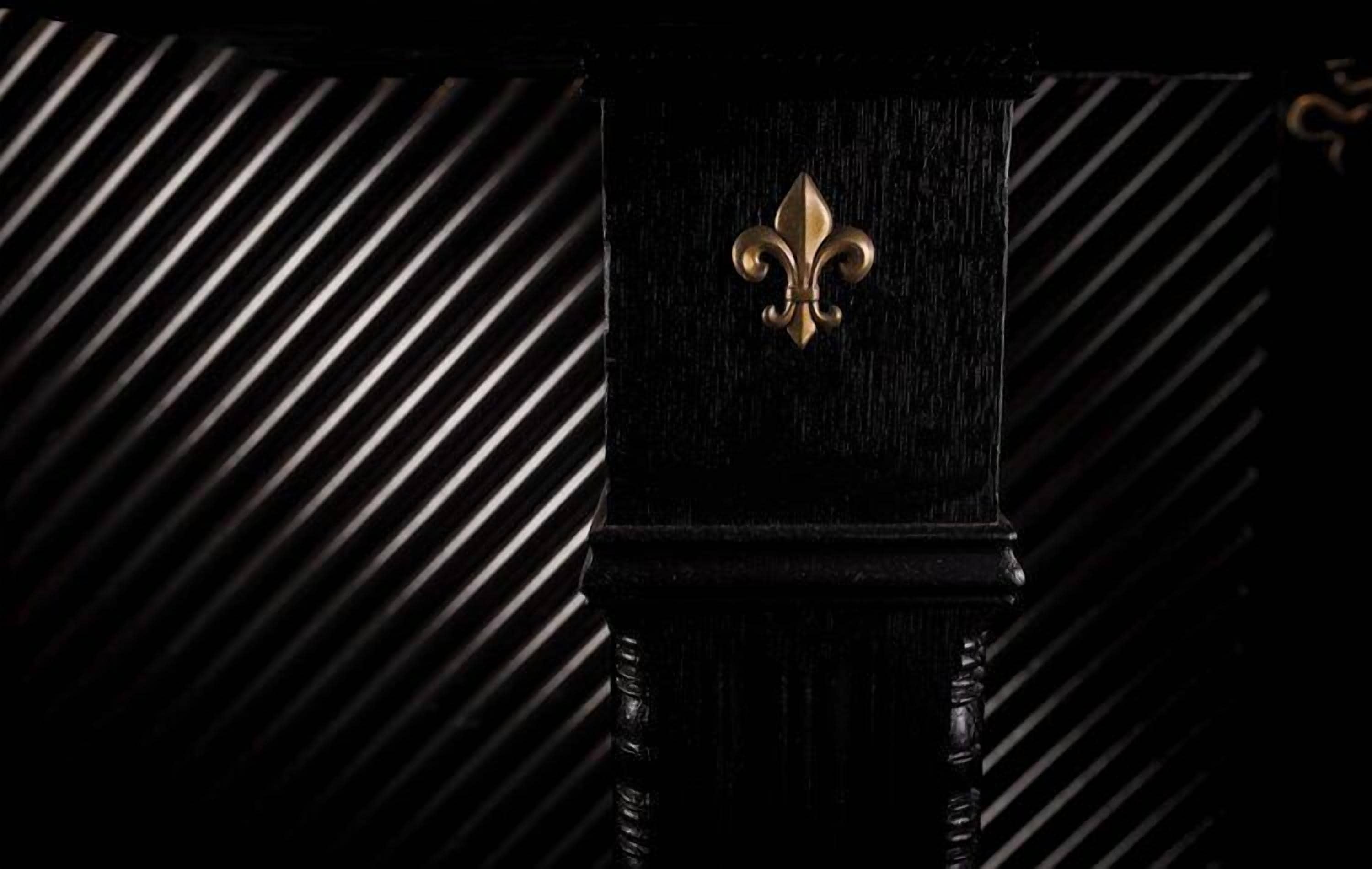 Une porte en bois noir ornée d’un écusson doré en forme de fleur de lys.