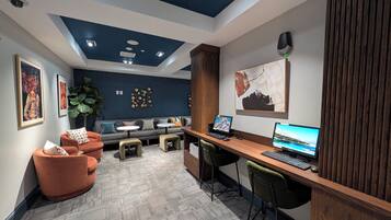 A modern office space with a dark blue ceiling, two desks with computers, a sofa with cushions, and a large plant.