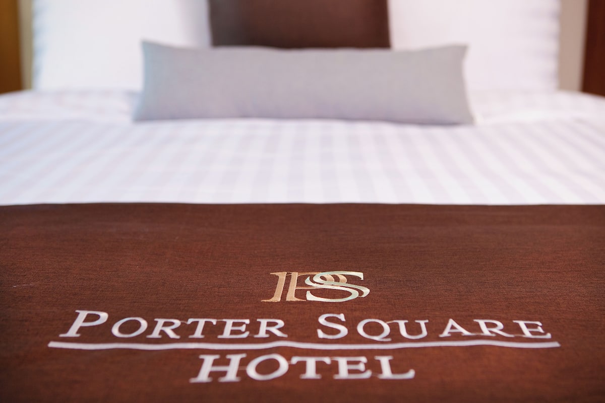 Una cama con una colcha blanca y una manta marrón con la inscripción "Porter Square Hotel".