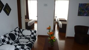 A hotel room with a sofa, a small table with flowers, a bed, and a chair.