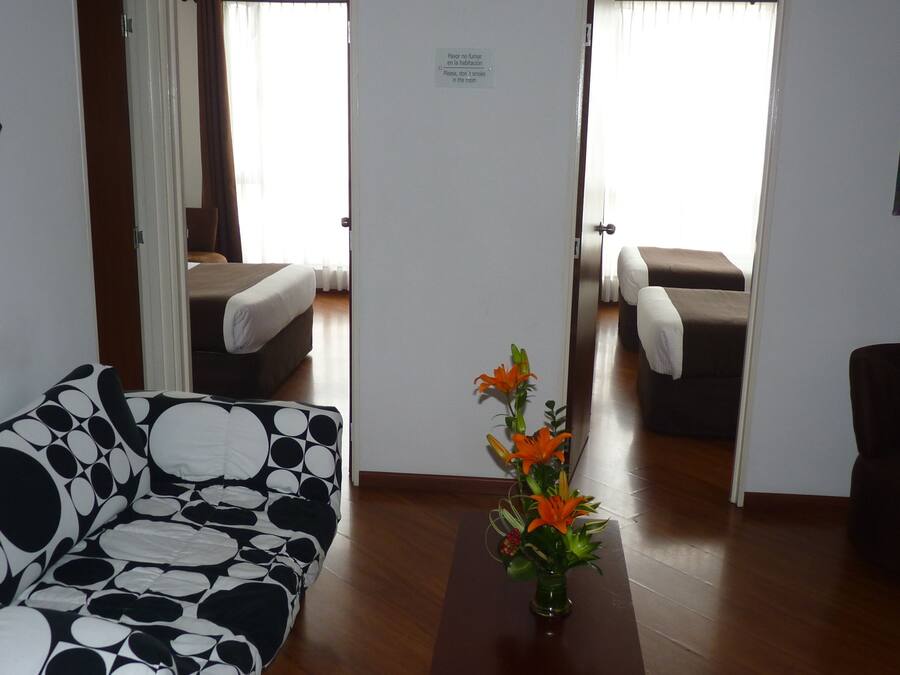 Una habitación de hotel con sofá, una mesita con flores, cama y una silla.