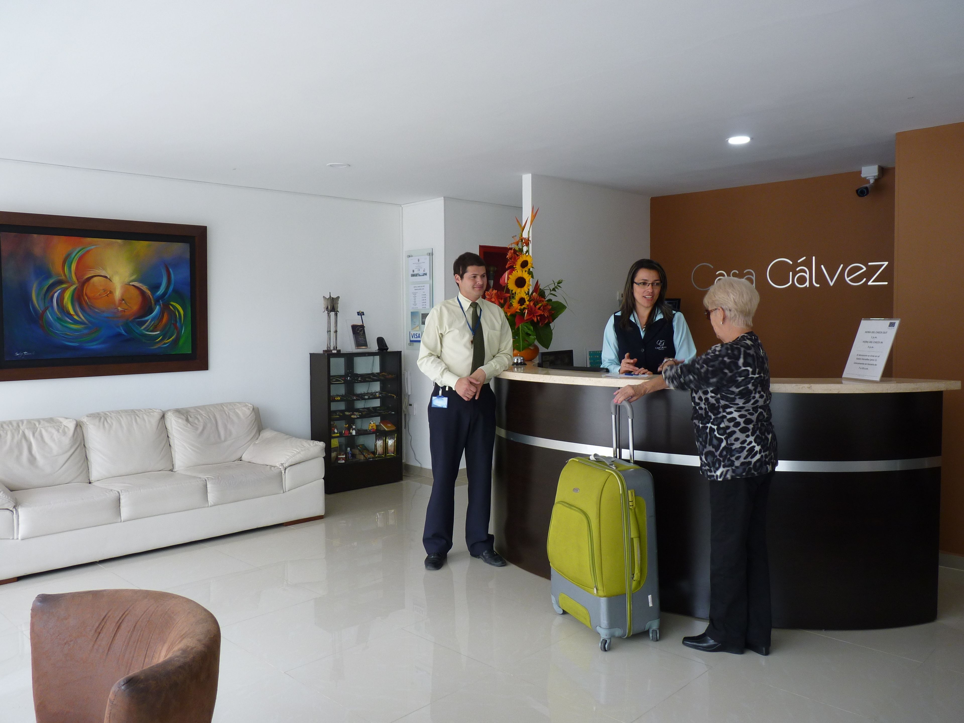 A reception area with a reception desk, a sofa, a coffee table, a painting, and a flower arrangement.