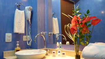 Une salle de bain avec un lavabo, deux porte-serviettes, un miroir, un vase à fleurs et des articles de toilette posés sur le comptoir.