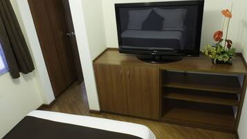 A hotel room with a bed, a TV on a wooden cabinet, and a potted plant.