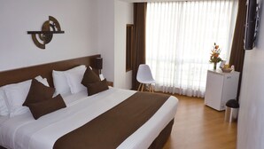 A hotel room with a large bed, a desk, a chair, and a window with curtains.