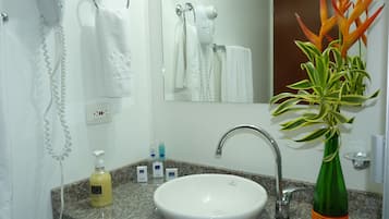 Un bany amb un lavabo blanc, un mirall, un suport per a tovalloles, un assecador d'eixugat i una planta decorativa en una ampolla.