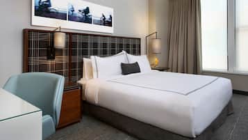 A hotel room with a large bed, a desk, a chair, a headboard with a grid pattern, and a window with curtains.