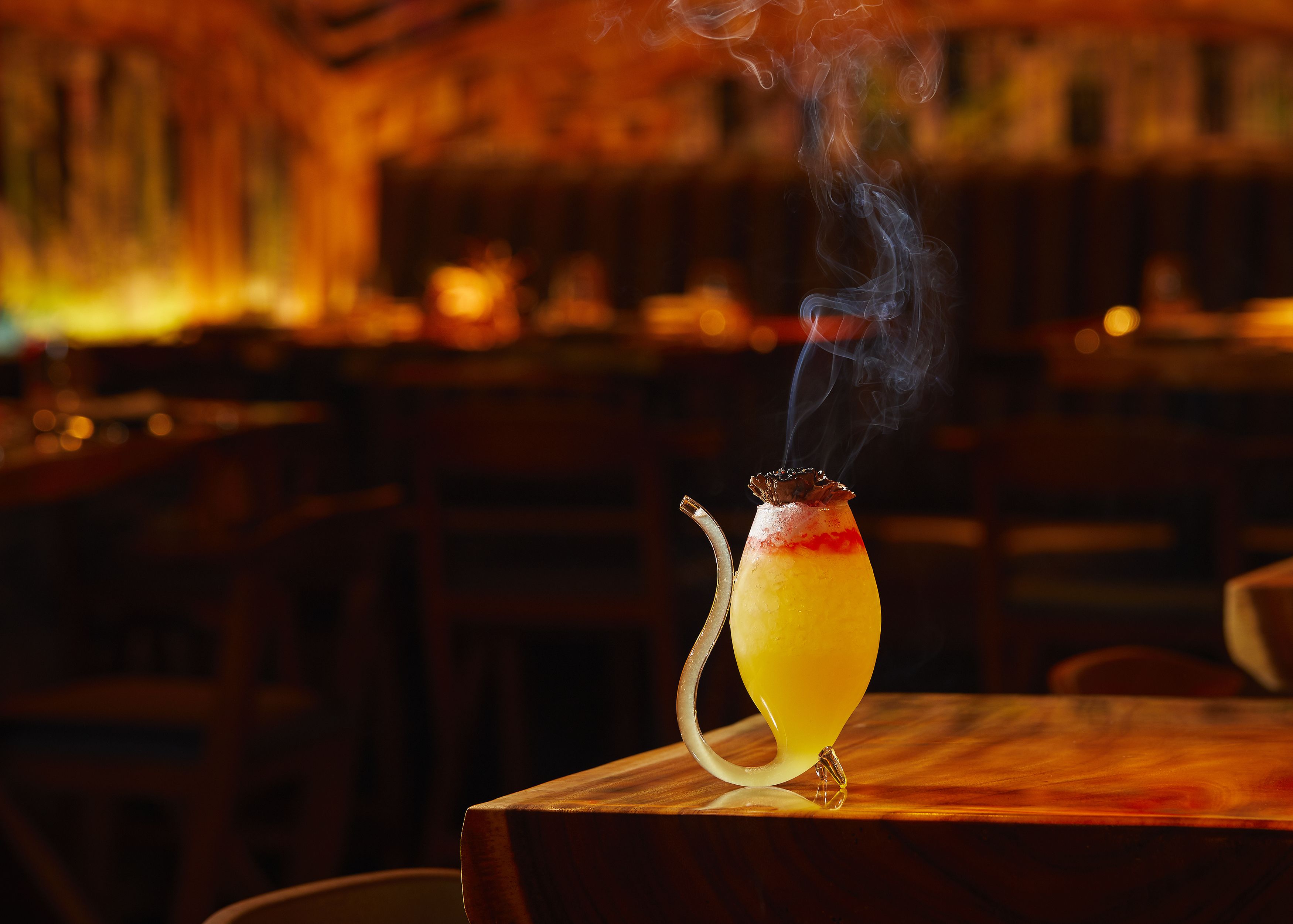 A cocktail on a wooden table in a dimly lit bar with a warm ambiance.