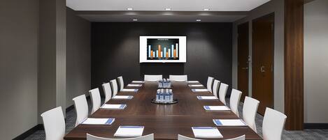 A conference room with a long table, white chairs, and a screen displaying a bar chart.