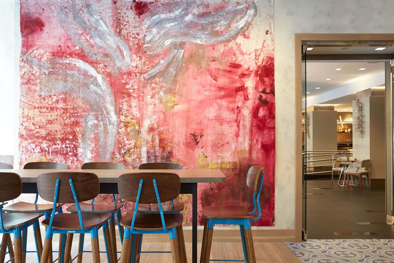 A modern dining area with a large abstract painting, wooden tables, and blue chairs.