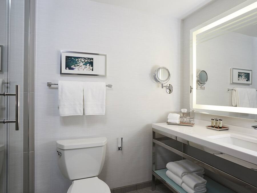 Une salle de bain moderne avec une douche à parois de verre, des toilettes blanches, un meuble-lavabo avec un grand miroir et des serviettes soigneusement rangées.
