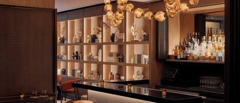 A bar area with a long counter, stools, and a variety of bottles and glasses.