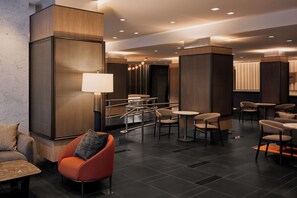 A modern hotel lobby with a seating area, a reception desk, and a large mirror.