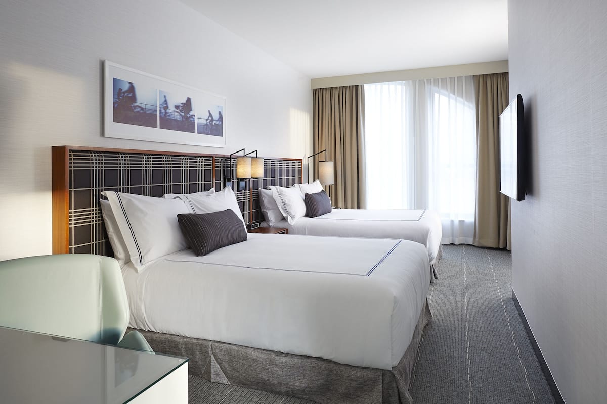 A hotel room with two beds, a desk, and a TV mounted on the wall.