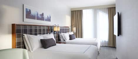 A hotel room with two beds, a desk, and a TV mounted on the wall.
