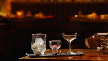 A bar setting with a glass of ice water, a small glass with a pink garnish, and a martini glass on a wooden table.
