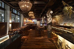 A restaurant with wooden flooring, multiple dining tables, and hanging chandeliers.