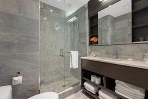 A modern bathroom with a glass-enclosed shower, marble walls, a large mirror, and a vanity with towels.