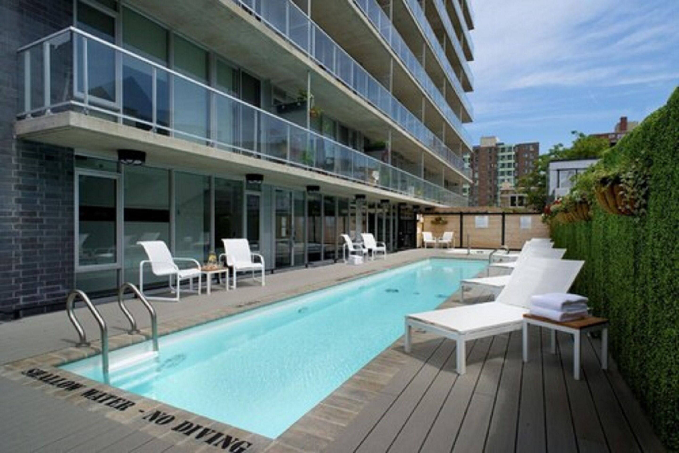 Un bâtiment moderne doté d’une piscine, de chaises longues et d’une balustrade en verre.