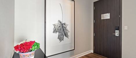 A hallway with a framed botanical print on the wall, a potted plant with red and white flowers, and a dark wooden door with a lock.