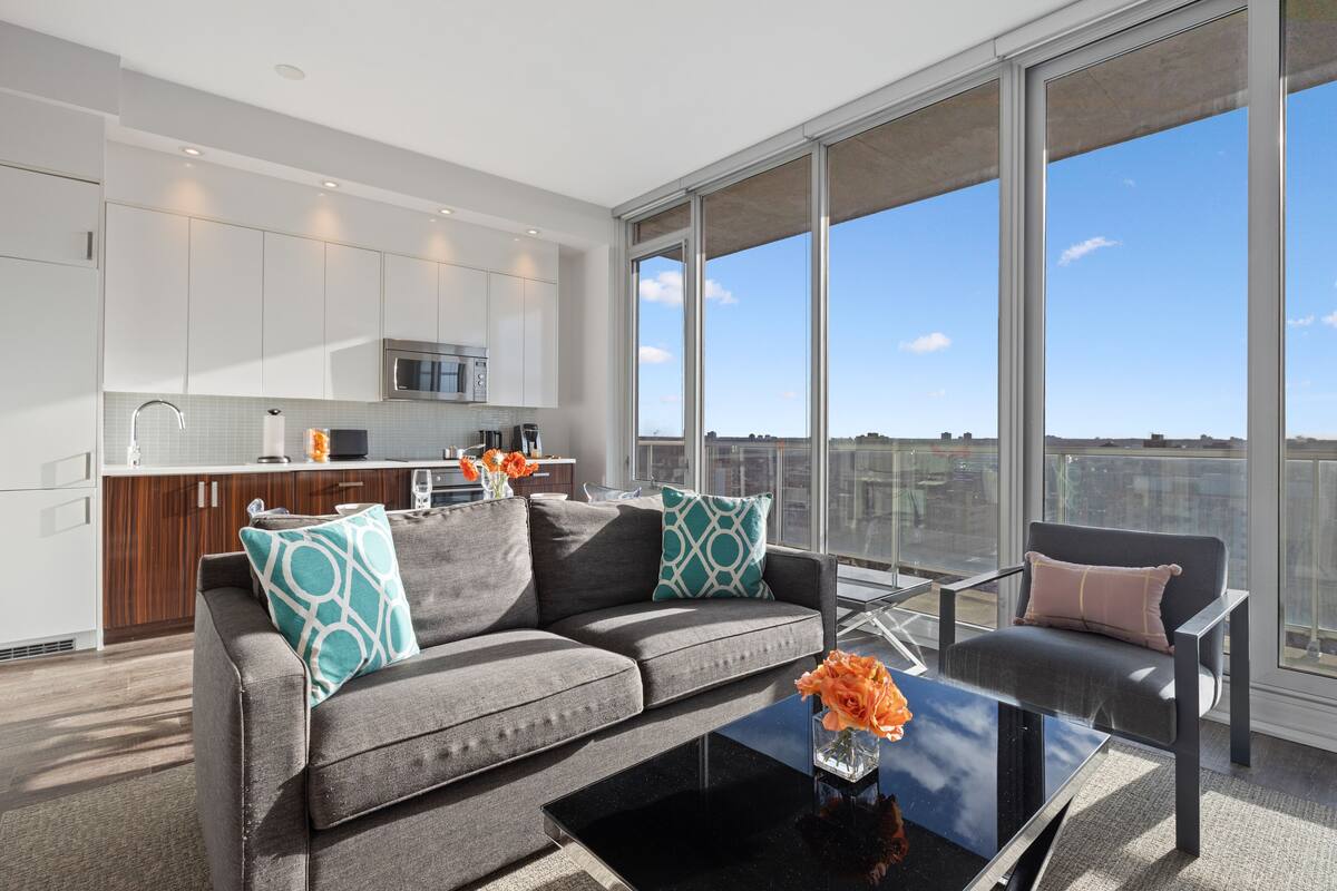 A modern living room with a sofa, coffee table, and a view of the city through large windows.