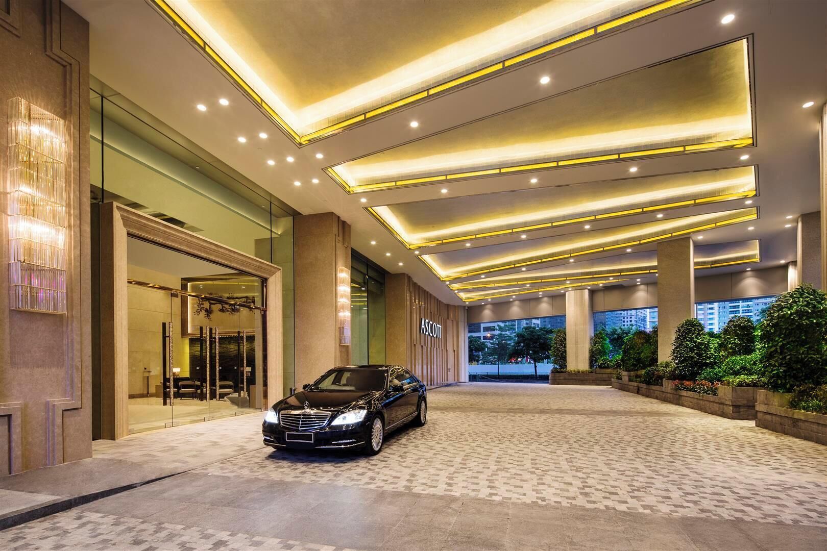 A modern hotel lobby with a car parked in the center, a large column, and a view of the cityscape through the windows.