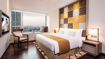 A hotel room with a large bed, a desk, a chair, a TV, and a city view.